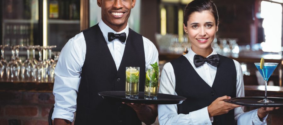 Portrait of waiter and waitress holding a serving tray with glass of cocktail